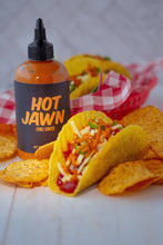 Load image into Gallery viewer, A gringo hard taco with Hot Jawn Chili Sauce, surrounded by tortilla chips, in front of a bottle of Hot Jawn Chili Sauce.