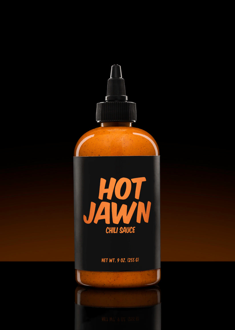 A bottle of Hot Jawn Chili Sauce on a black background with an orange sunset gradient