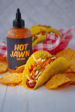 Load image into Gallery viewer, A gringo hard taco with Hot Jawn Chili Sauce, surrounded by tortilla chips, in front of a bottle of Hot Jawn Chili Sauce. 
