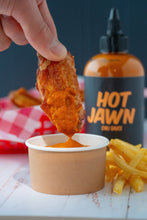 Load image into Gallery viewer, A man dipping a chicken flat in Hot Jawn Chili Sauce with fries on the side and a bottle of Hot Jawn Chili Sauce in the background.
